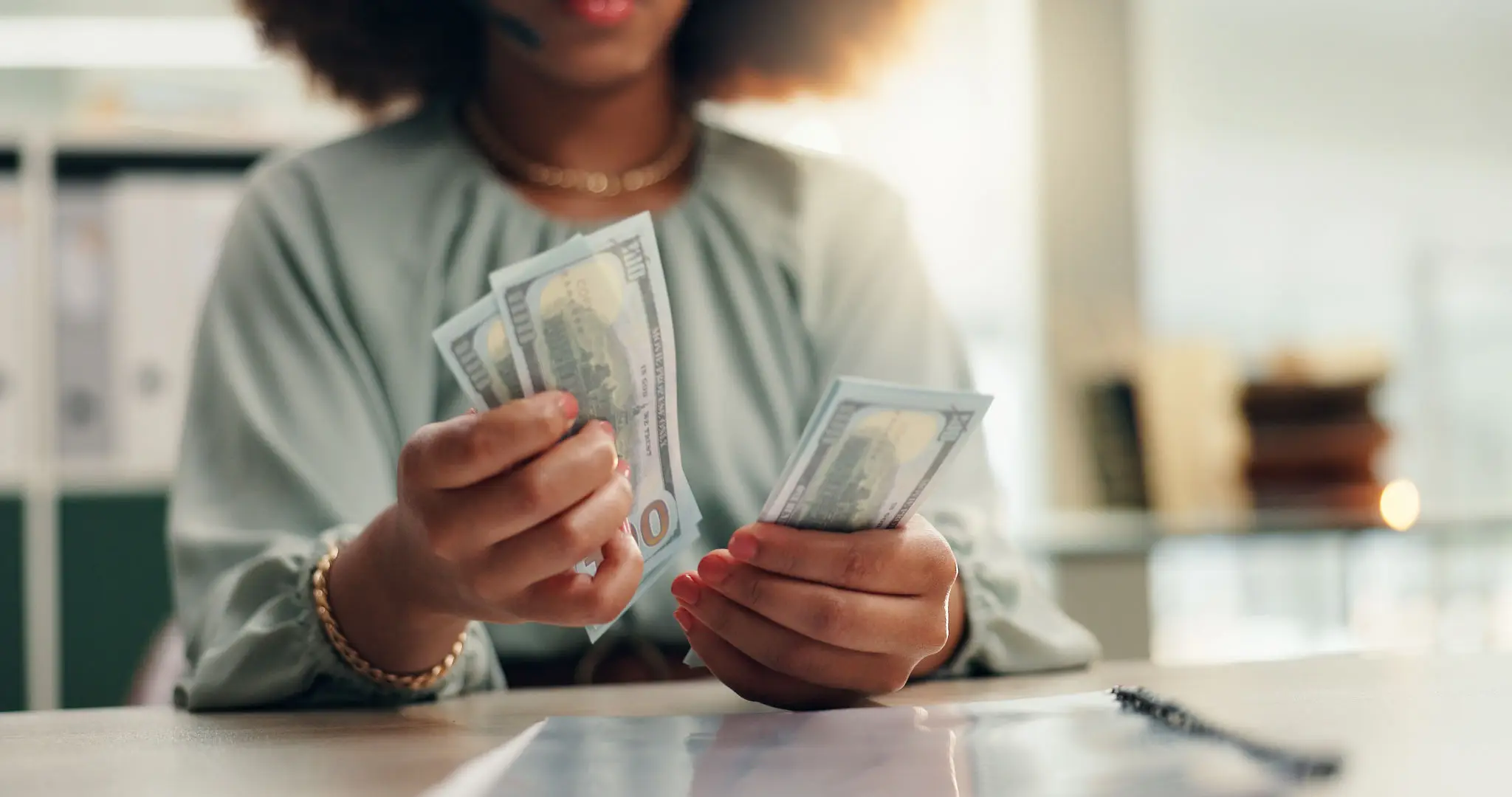 Person counting US dollar bills at desk